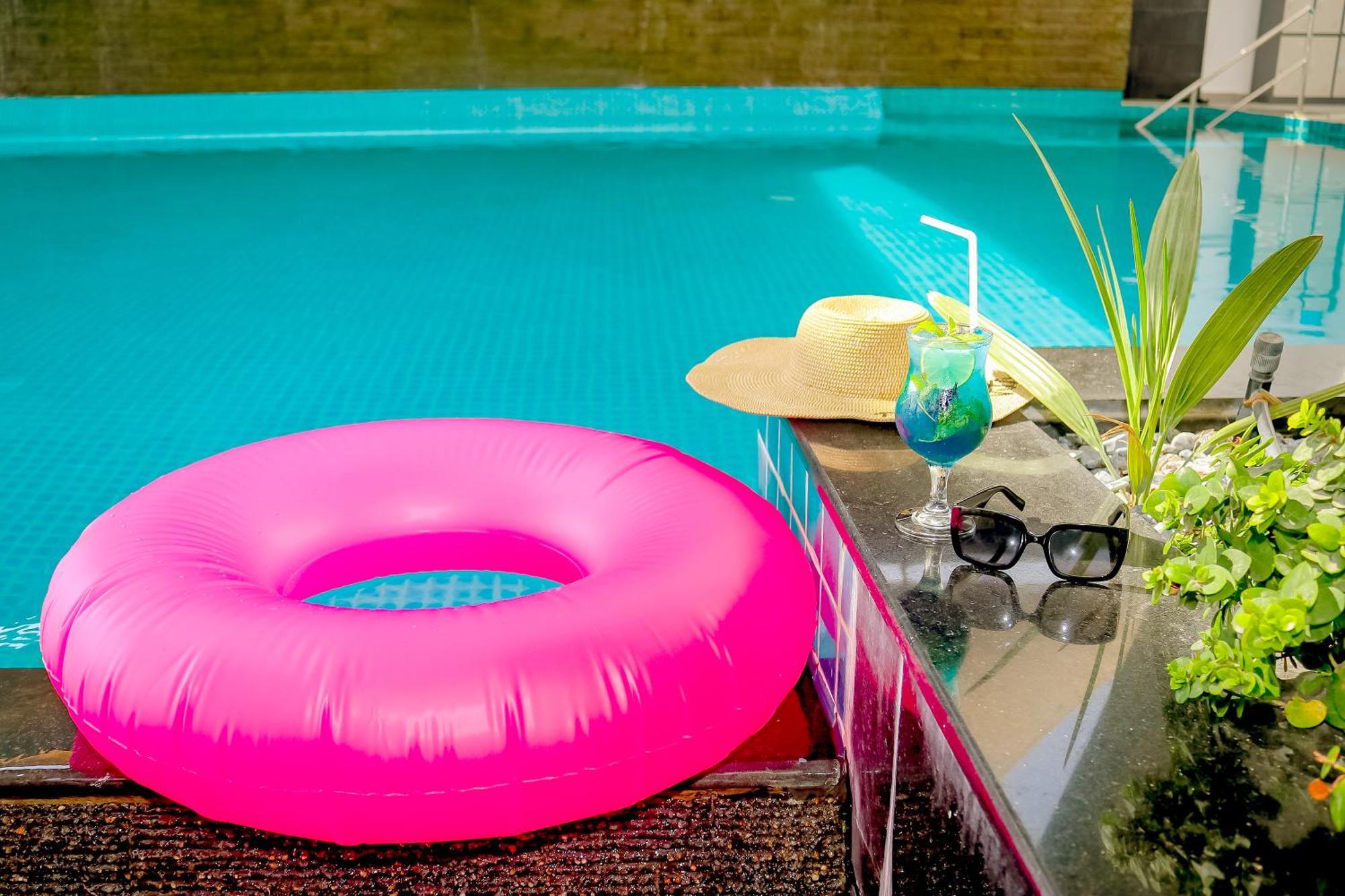 Lagoona Beach Luxury Resort And Spa Manama Exteriör bild The photo shows a vibrant and inviting scene by a swimming pool. In the foreground, there is a large pink inflatable float and a stylish straw hat. Next to the float, a refreshing cocktail in a glass is displayed, complete with a straw and garnishes.