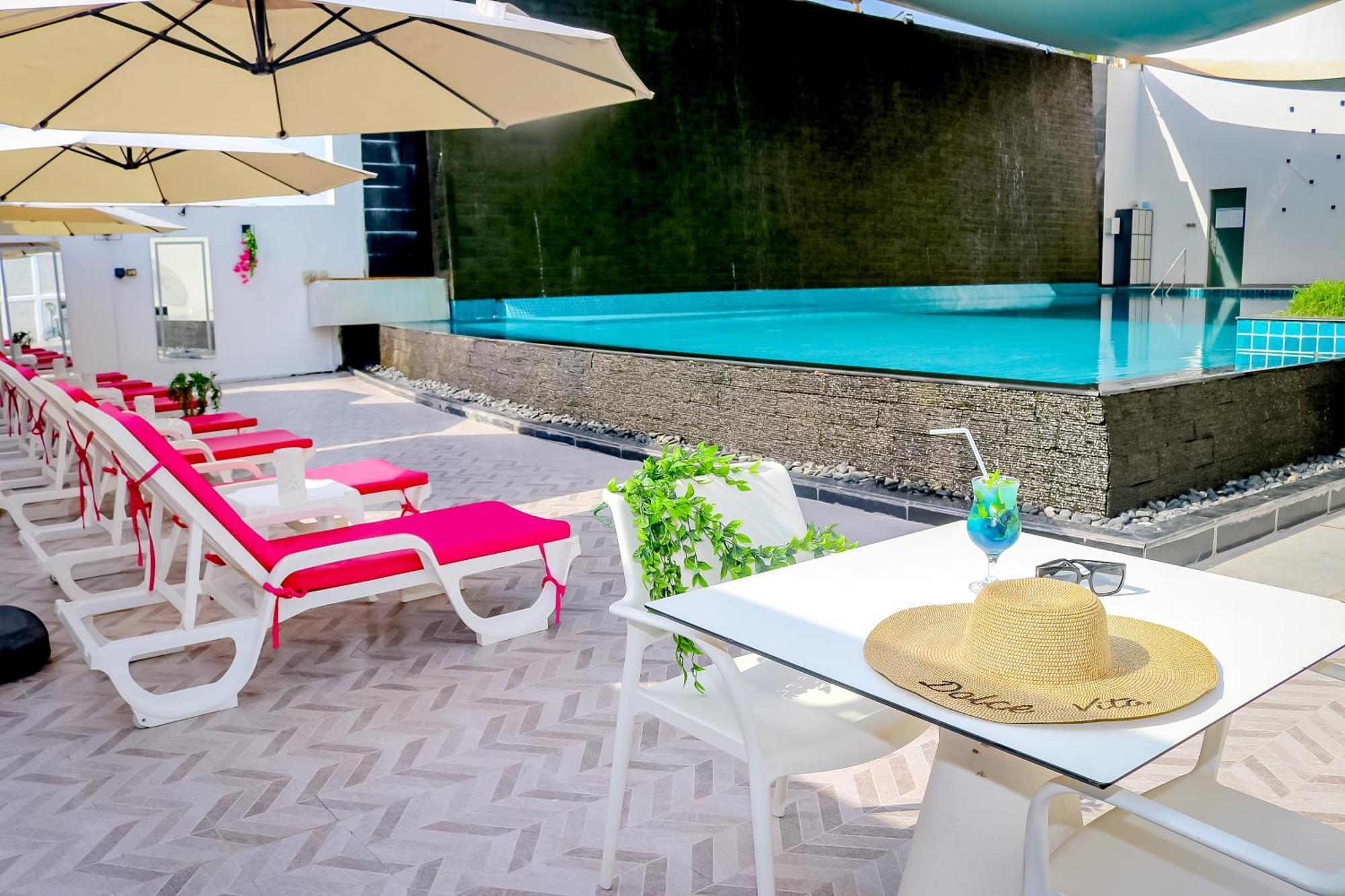 Lagoona Beach Luxury Resort And Spa Manama Exteriör bild The photo shows a sunny poolside area with bright red lounge chairs arranged neatly beside a swimming pool. There are large beige umbrellas providing shade. A small table is set up with a straw hat and a colorful drink, suggesting a relaxed, tropical