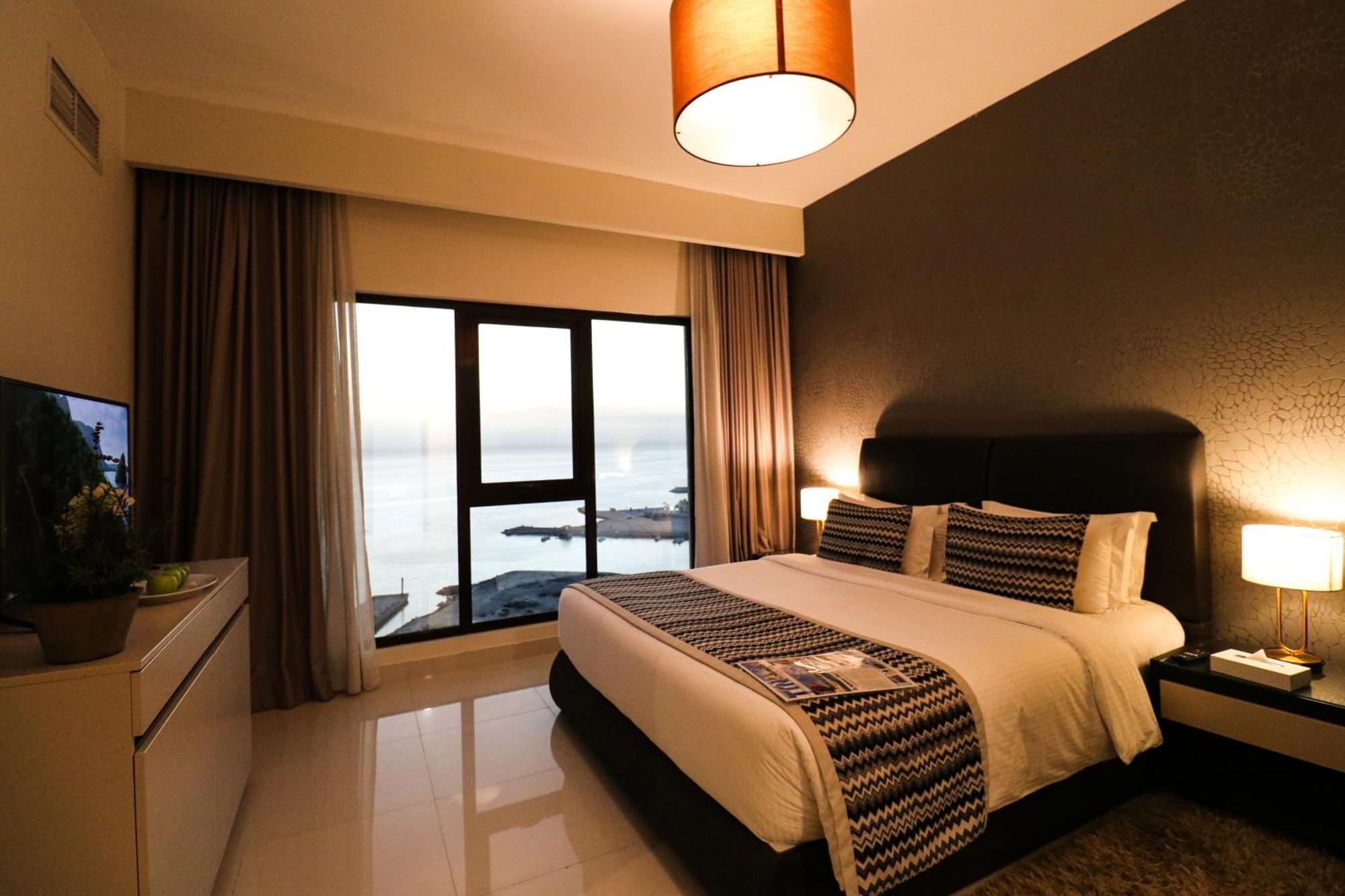 Lagoona Beach Luxury Resort And Spa Manama Exteriör bild The photo shows a modern hotel room featuring a neatly made bed with decorative pillows. The room has a stylish design with a dark accent wall and a large window that offers a view of the outdoors. Natural light comes in, giving the space a bright an