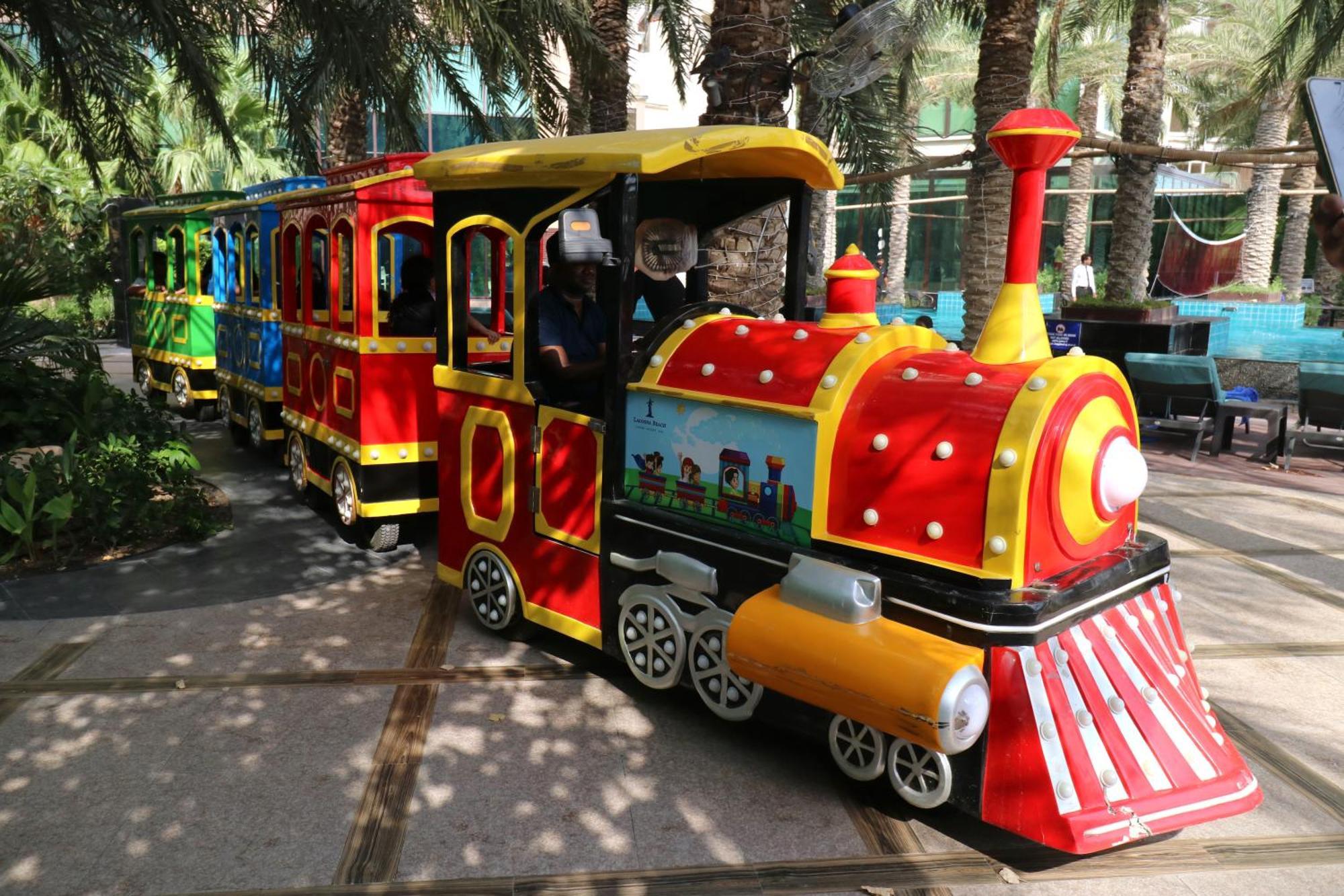 Lagoona Beach Luxury Resort And Spa Manama Exteriör bild The photo shows a colorful miniature train. It features a vibrant design with bright red, yellow, and blue colors. The front of the train resembles a classic steam engine, complete with a prominent smokestack. The train is designed to resemble a fun 