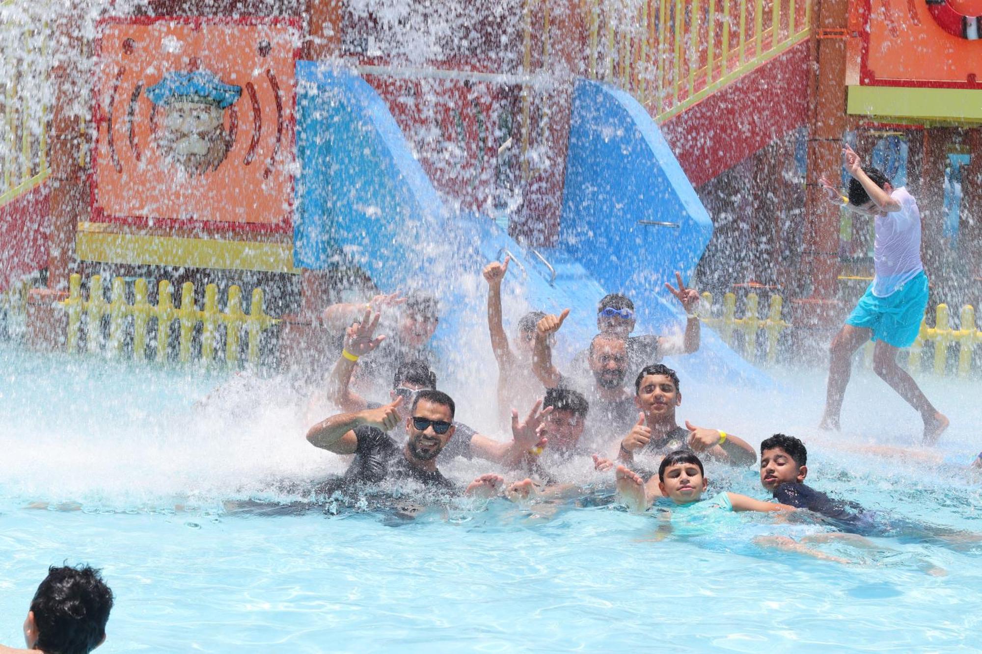 Lagoona Beach Luxury Resort And Spa Manama Exteriör bild The photo shows a lively scene at a water park or pool area. Several people, including adults and children, are enjoying themselves in the water, splashing and posing for the camera. Water is cascading down, creating a refreshing atmosphere. In the b