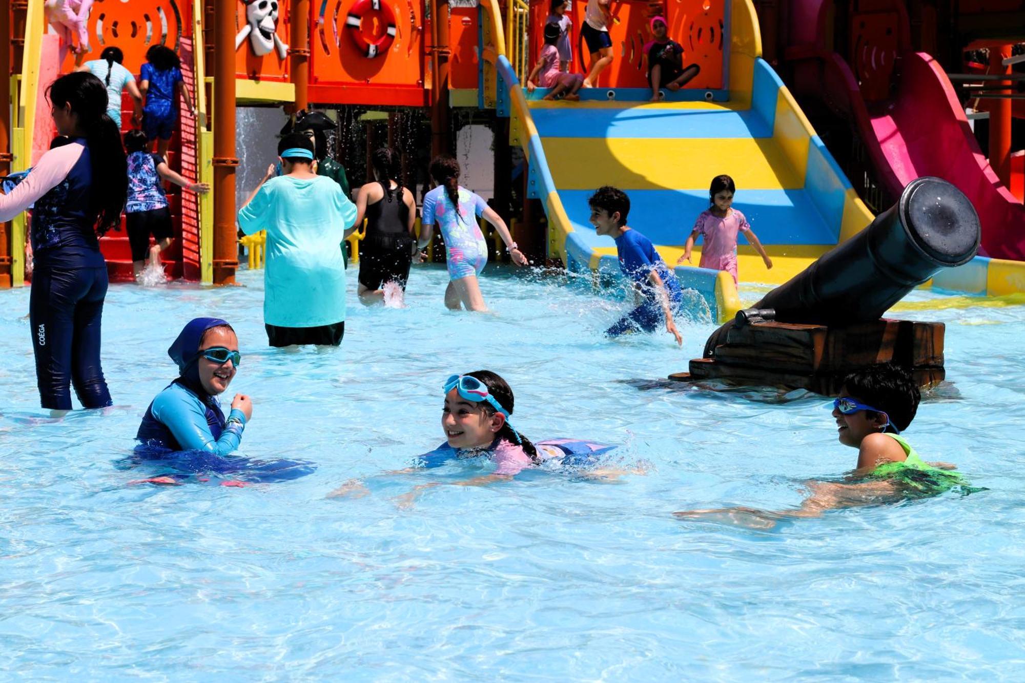 Lagoona Beach Luxury Resort And Spa Manama Exteriör bild The photo shows a vibrant water park scene with several children playing in a shallow pool. Some are swimming and splashing around, while others are playing on colorful slides in the background. The atmosphere is lively and cheerful, with kids of var