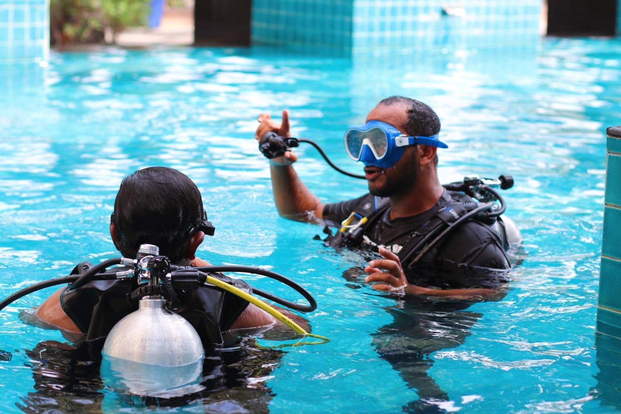 Lagoona Beach Luxury Resort And Spa Manama Exteriör bild The photo shows two divers in a pool. One diver is wearing a scuba mask and is speaking to the other diver, who is also equipped with scuba gear. They appear to be engaged in a discussion, possibly related to diving instructions or safety. The water 