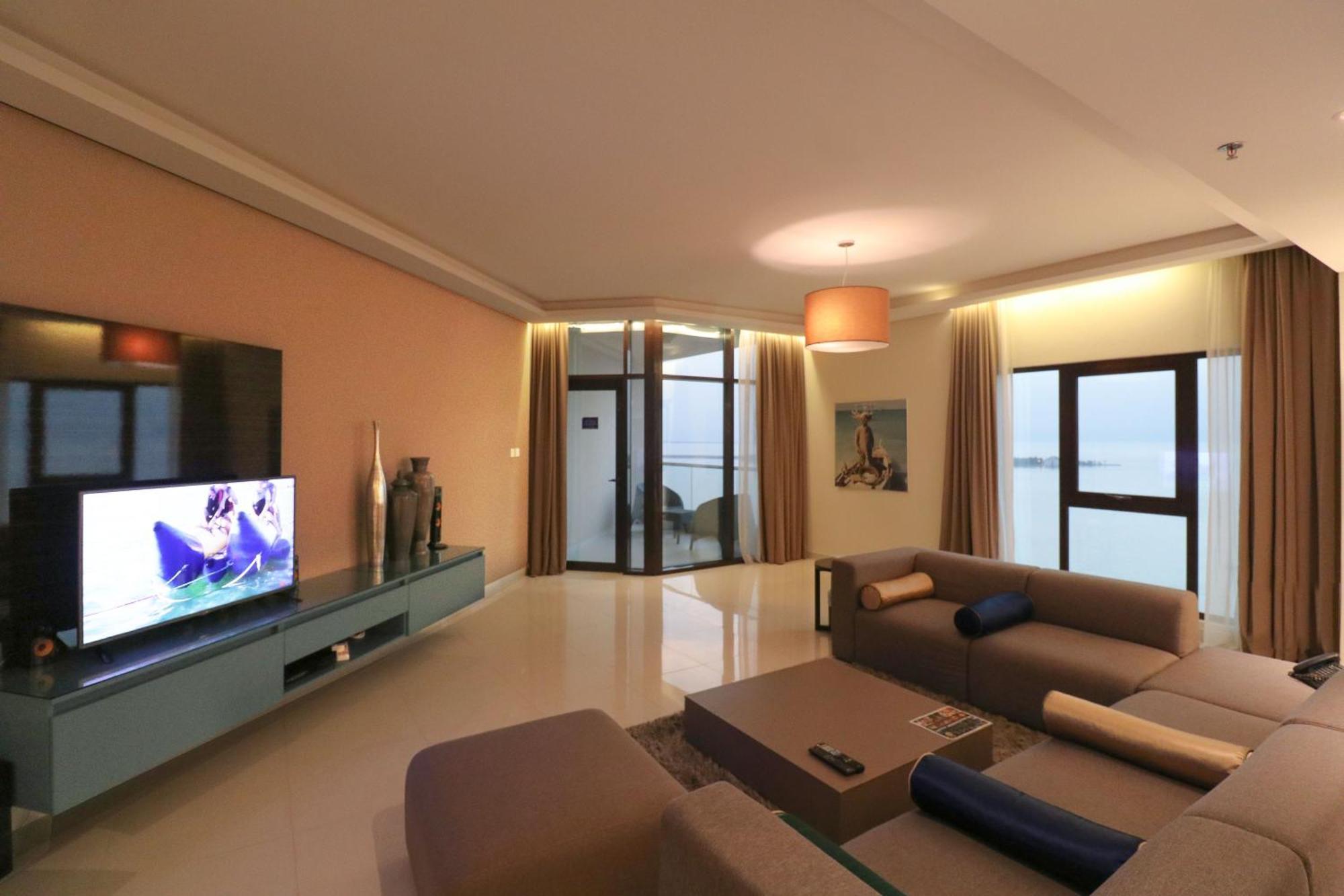 Lagoona Beach Luxury Resort And Spa Manama Exteriör bild The photo shows a modern living room with a sleek design. There is a large wall-mounted television on a contemporary entertainment unit, with decorative items placed beside it. The room features a comfortable sectional sofa in light tones, with a cof