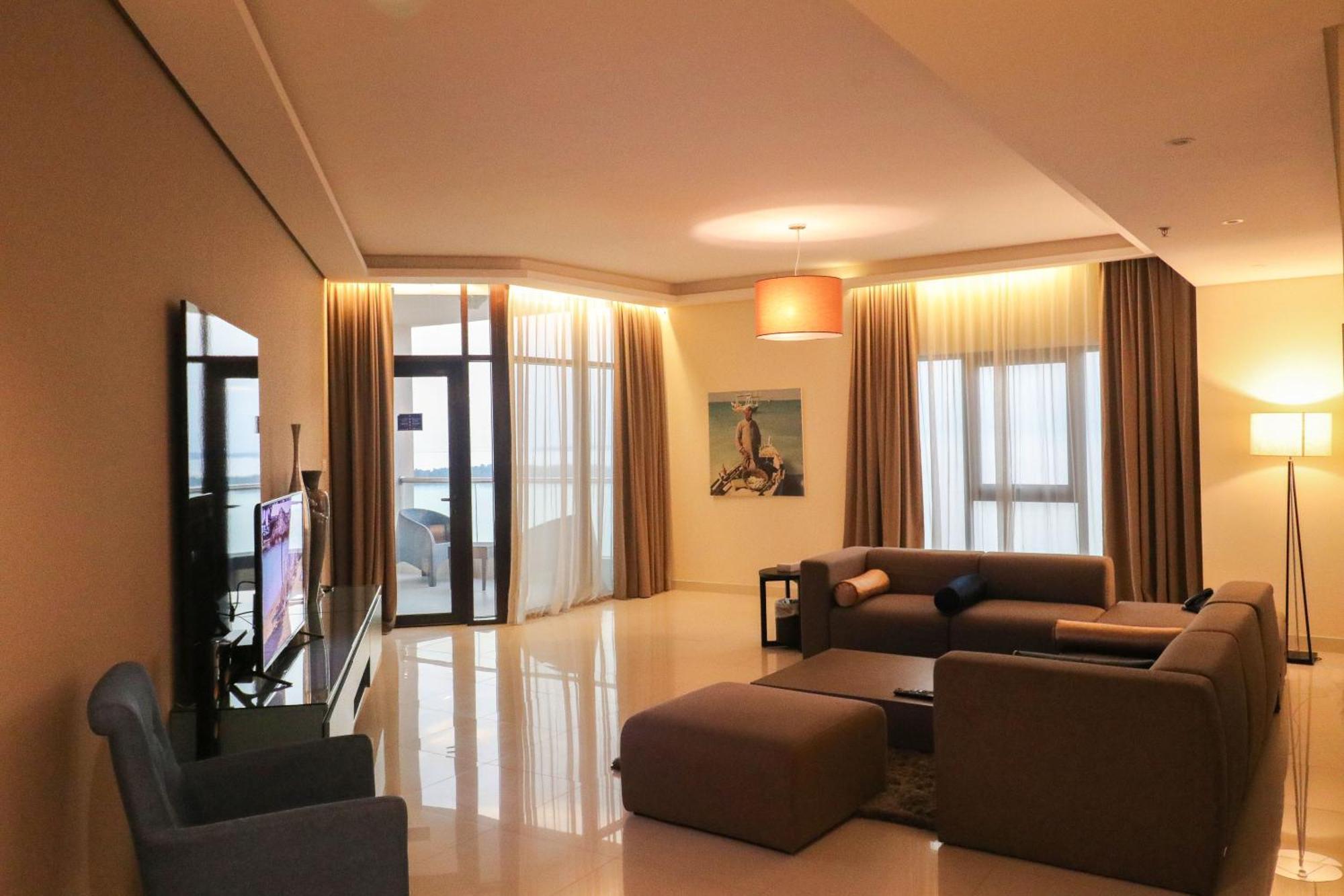 Lagoona Beach Luxury Resort And Spa Manama Exteriör bild The photo shows a modern living room with a spacious and elegant design. It features a large couch in neutral tones, a soft ottoman, and a stylish coffee table. The walls are painted in a light color, and there are large windows with sheer curtains a