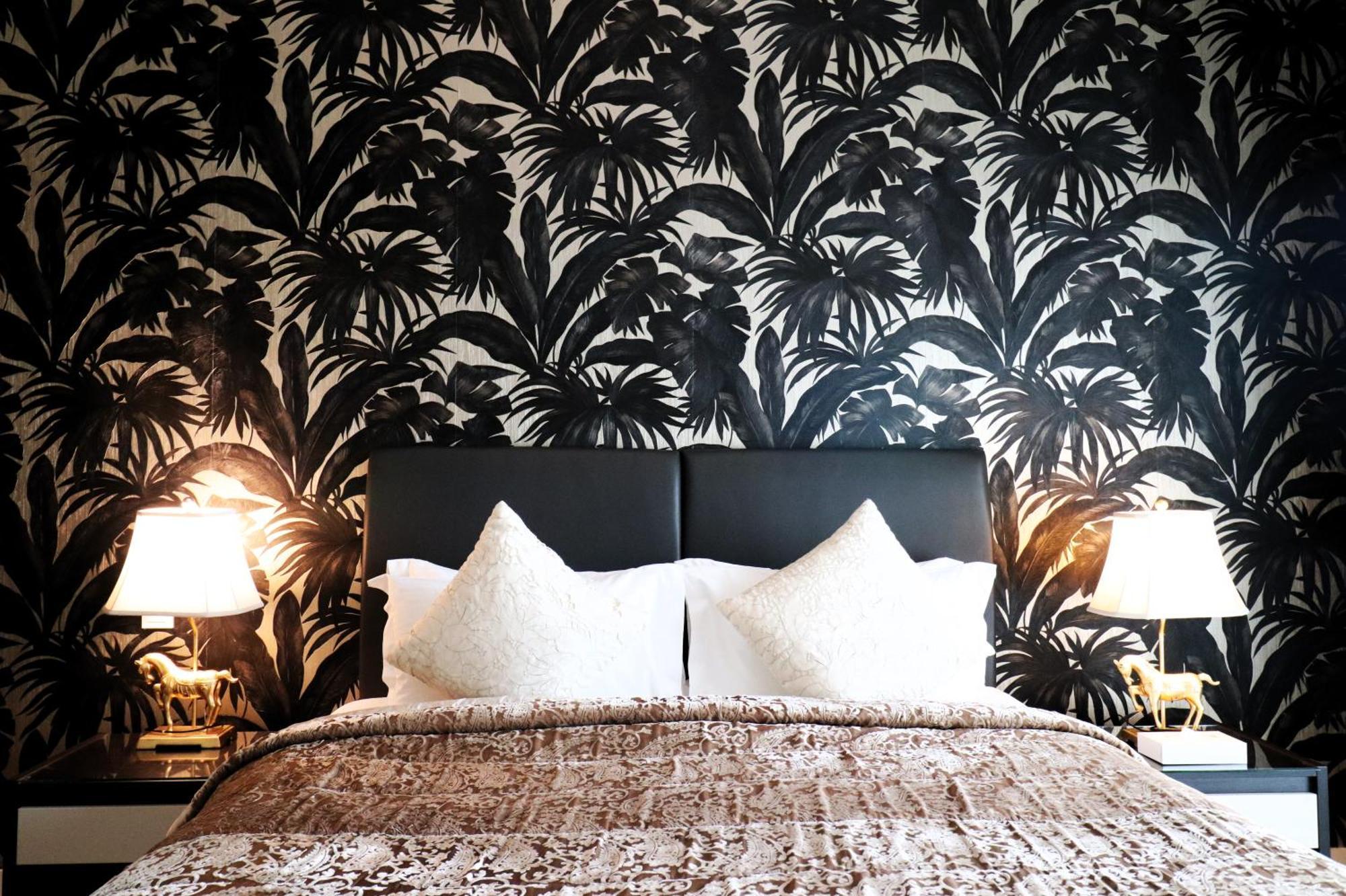 Lagoona Beach Luxury Resort And Spa Manama Exteriör bild The photo depicts a stylish bedroom featuring a distinctive wall covered in a black and white tropical foliage wallpaper. The bed has a modern black headboard and is adorned with white pillows, creating a clean and elegant look. A textured brown thro