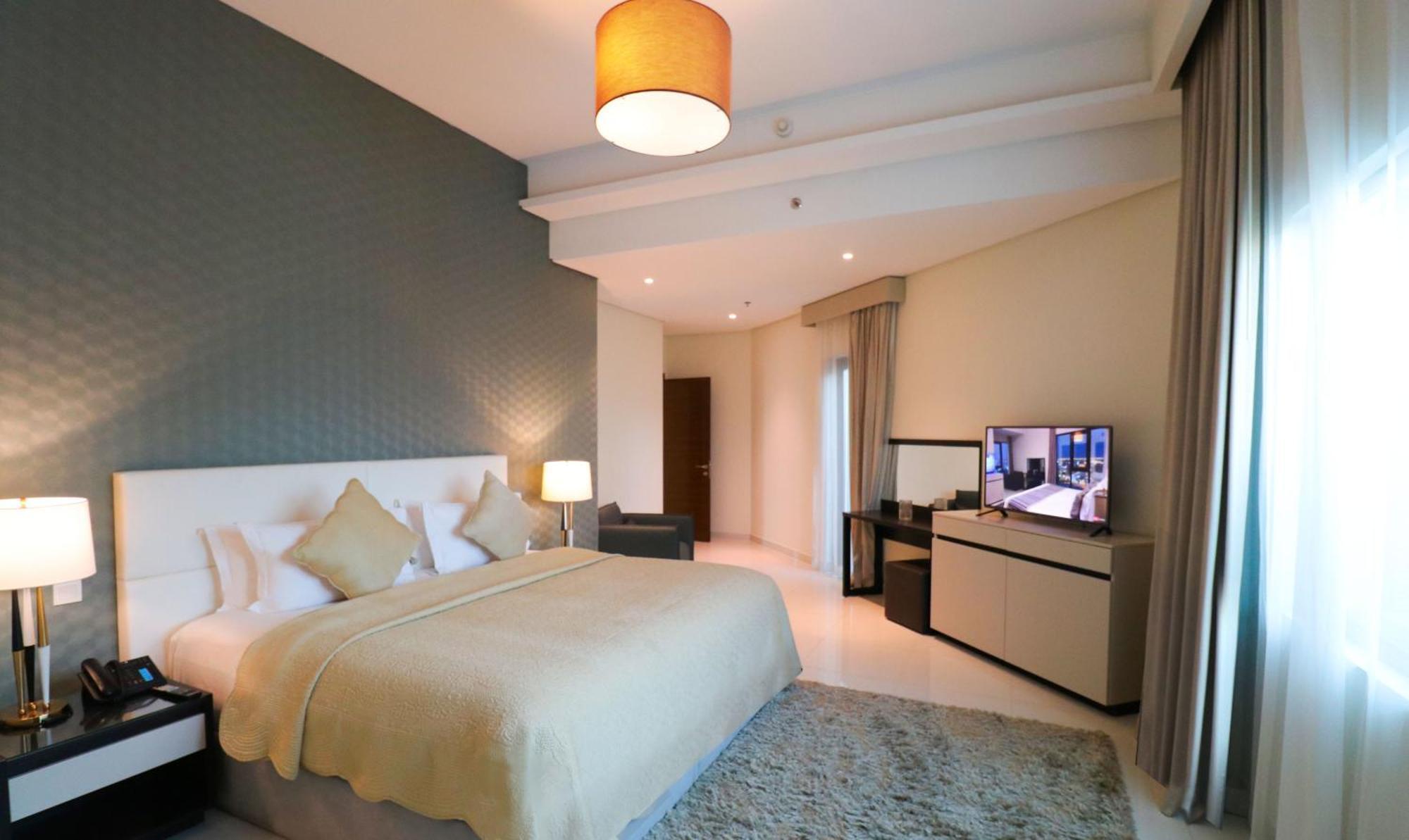Lagoona Beach Luxury Resort And Spa Manama Exteriör bild The photo shows a modern hotel room featuring a large bed with a light-colored blanket and decorative pillows. The walls are painted in a subtle shade, and there is a textured accent wall behind the bed. On one side, a bedside lamp provides warm ligh